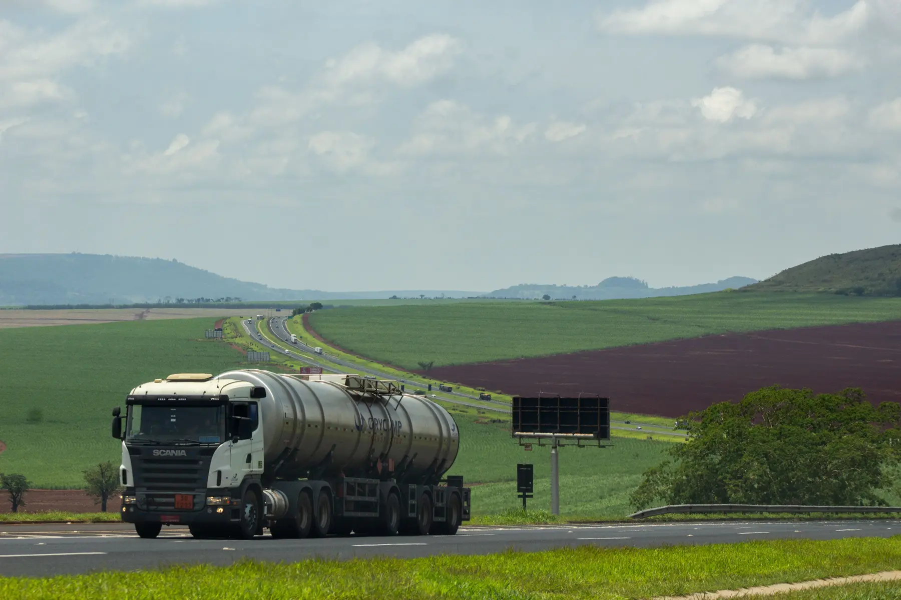 Caminhão tanque em rodovia com plantação ao fundo